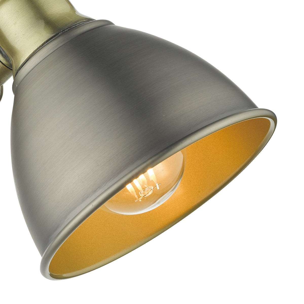 Close-up of a brushed antique brass lamp shade with a gold interior and an illuminated bulb.