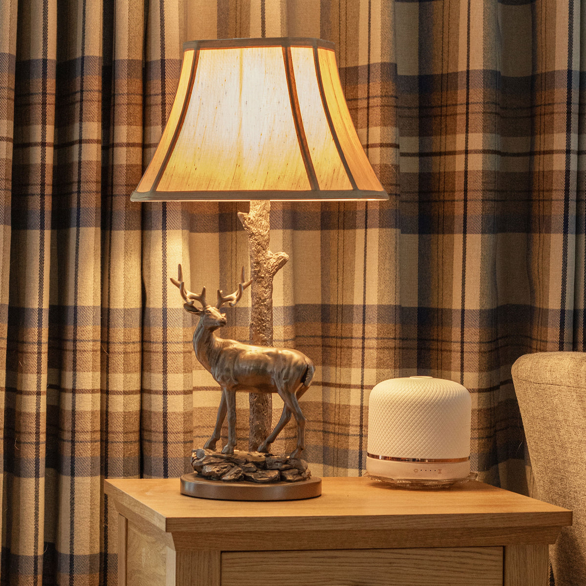 A deer-shaped lamp and a white diffuser on a wooden nightstand, with plaid curtains in the background.