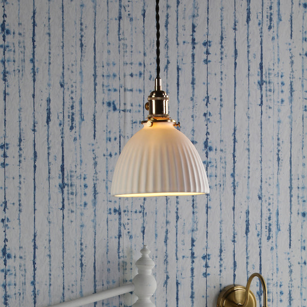 White fluted dome pendant light with brass accents, hanging against a blue and white striped wall.
