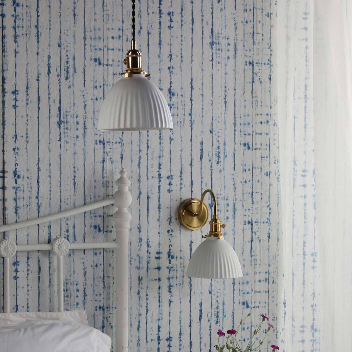 A white bed frame with a white duvet and pillows, with a blue and white striped wallpaper behind it.