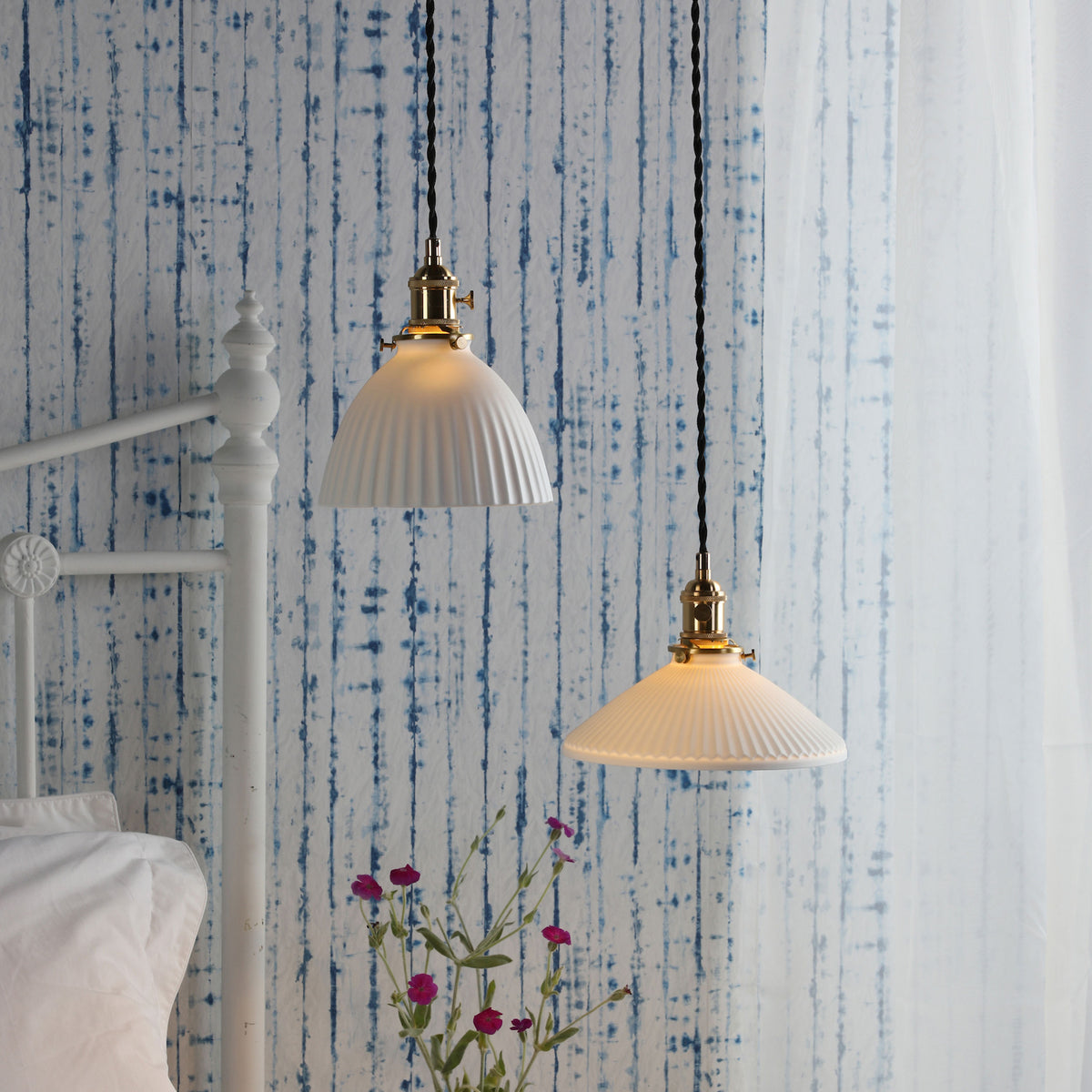 Two white fluted pendant lights with brass fittings hang against a blue and white striped wall.