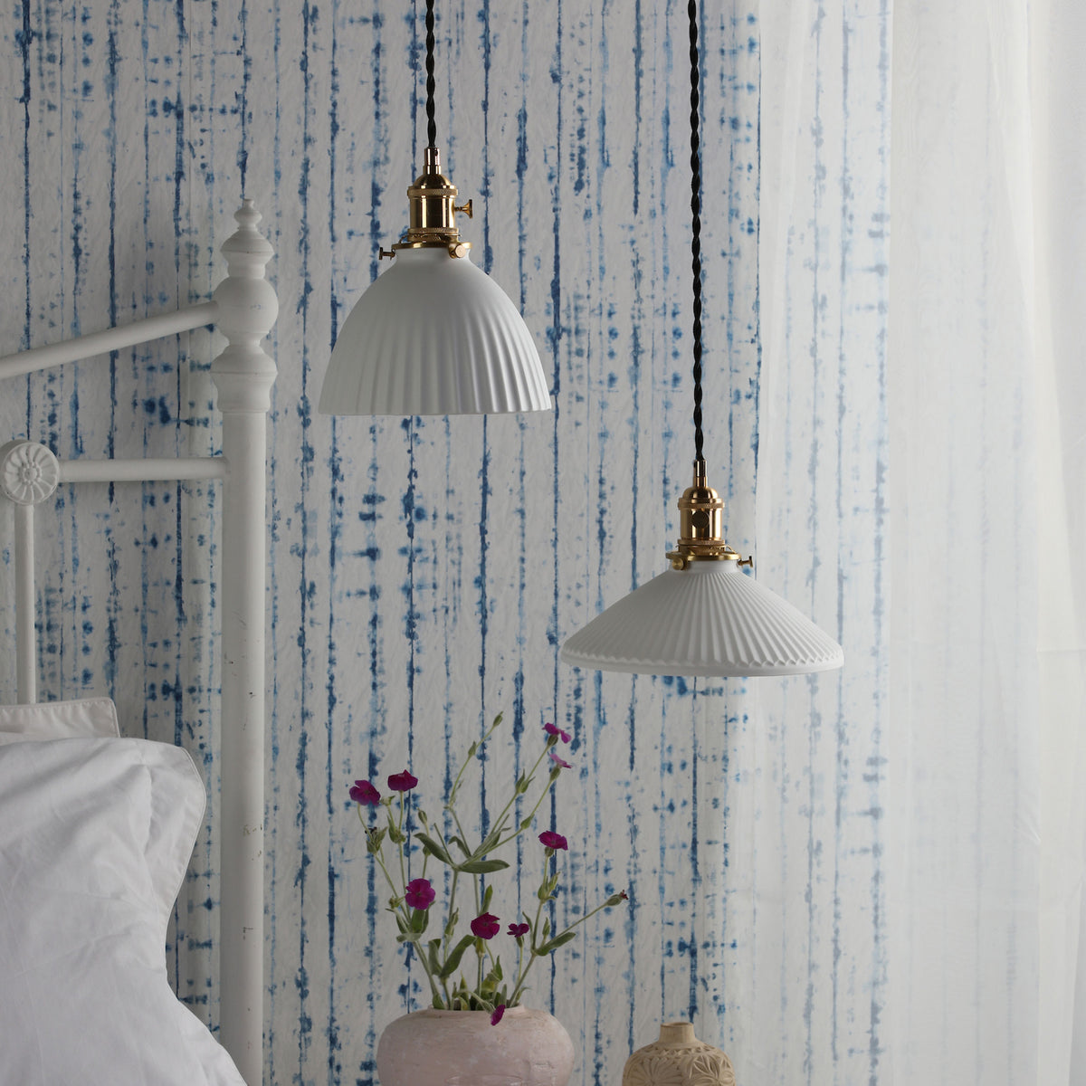 Two white fluted pendant lights with brass fittings hang against a blue and white striped wall.