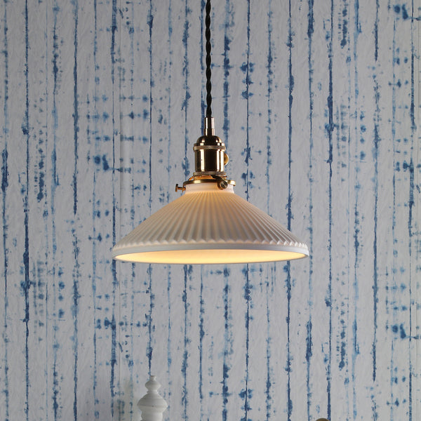 A white fluted pendant light with a brass fixture hangs against a blue and white striped wall.