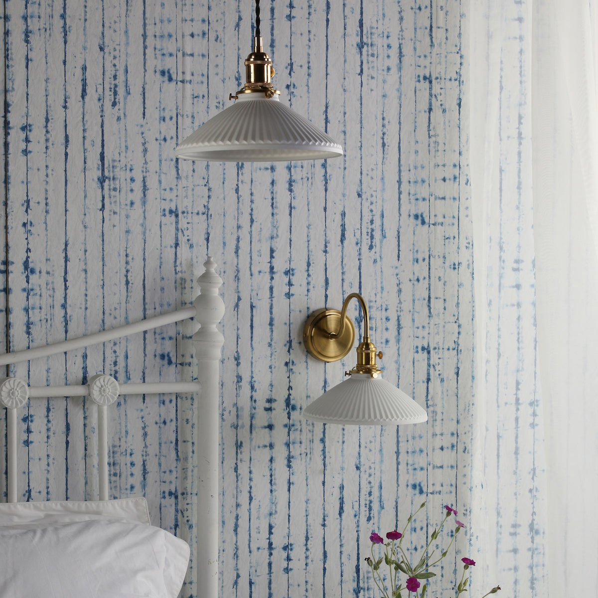 Bedroom with blue striped wallpaper, white bed frame, and two white and brass light fixtures.