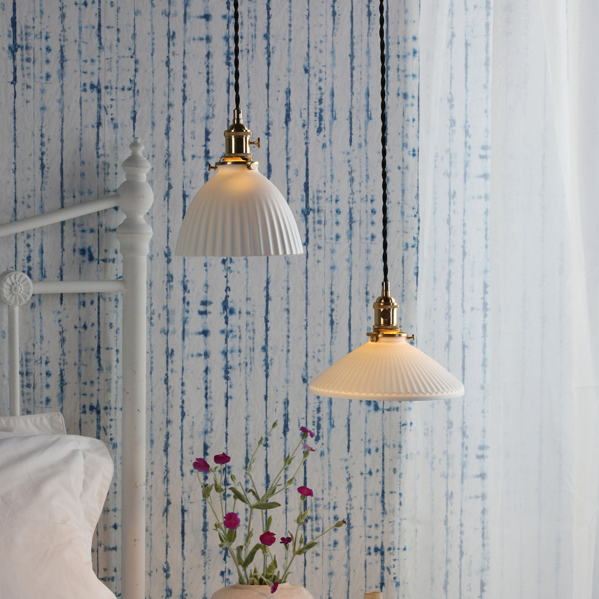 Two white fluted pendant lights with brass fittings hang against a blue and white striped wall.