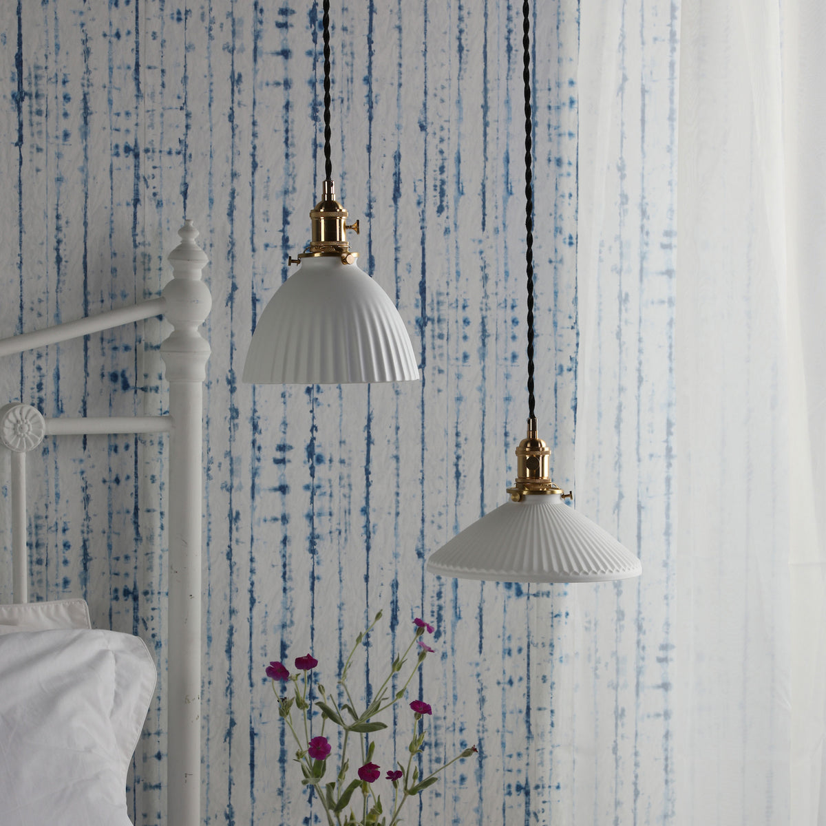 Two white fluted pendant lights with brass fittings hang against a blue and white striped wall.