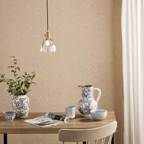 A dining table with a vase of flowers, a pitcher, and bowls, under a hanging glass lamp.