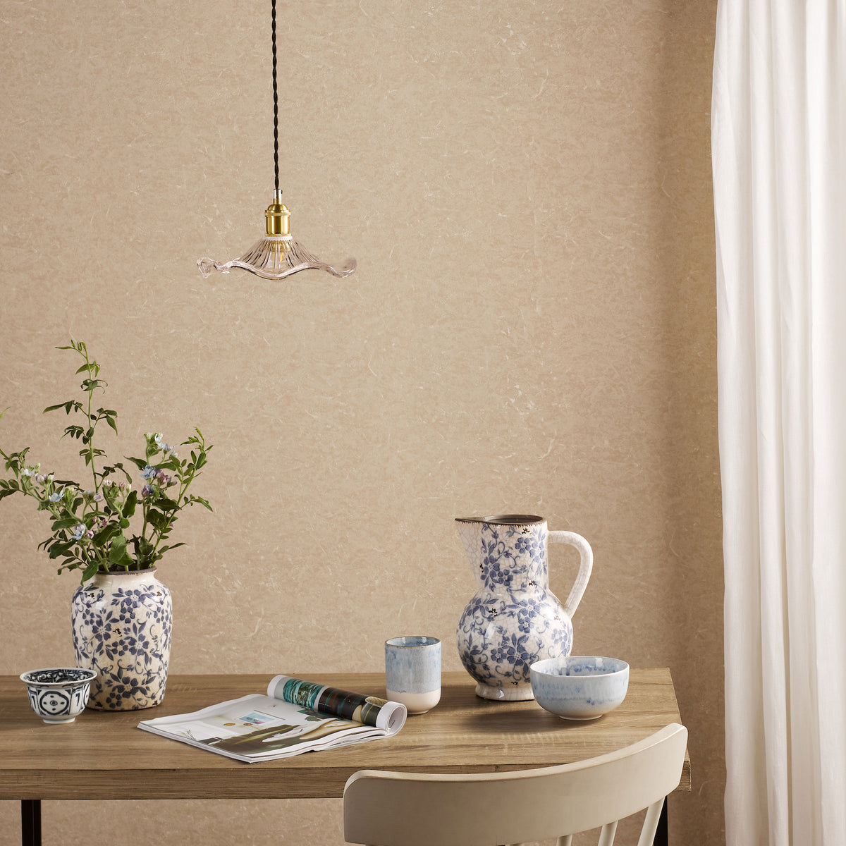 Dining table with blue and white floral ceramics, a magazine, and a light fixture.
