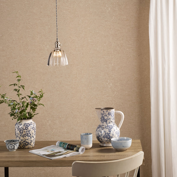 A wooden table with a vase of flowers, a pitcher, and bowls, all with blue floral patterns. A light hangs above.