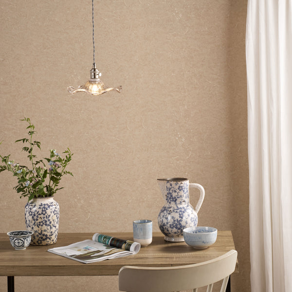 A dining table with a vase of flowers, a pitcher, and bowls, under a decorative pendant light.
