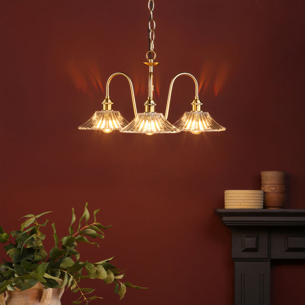 A three-light brass chandelier with fluted glass shades illuminates a dark red wall above a fireplace.