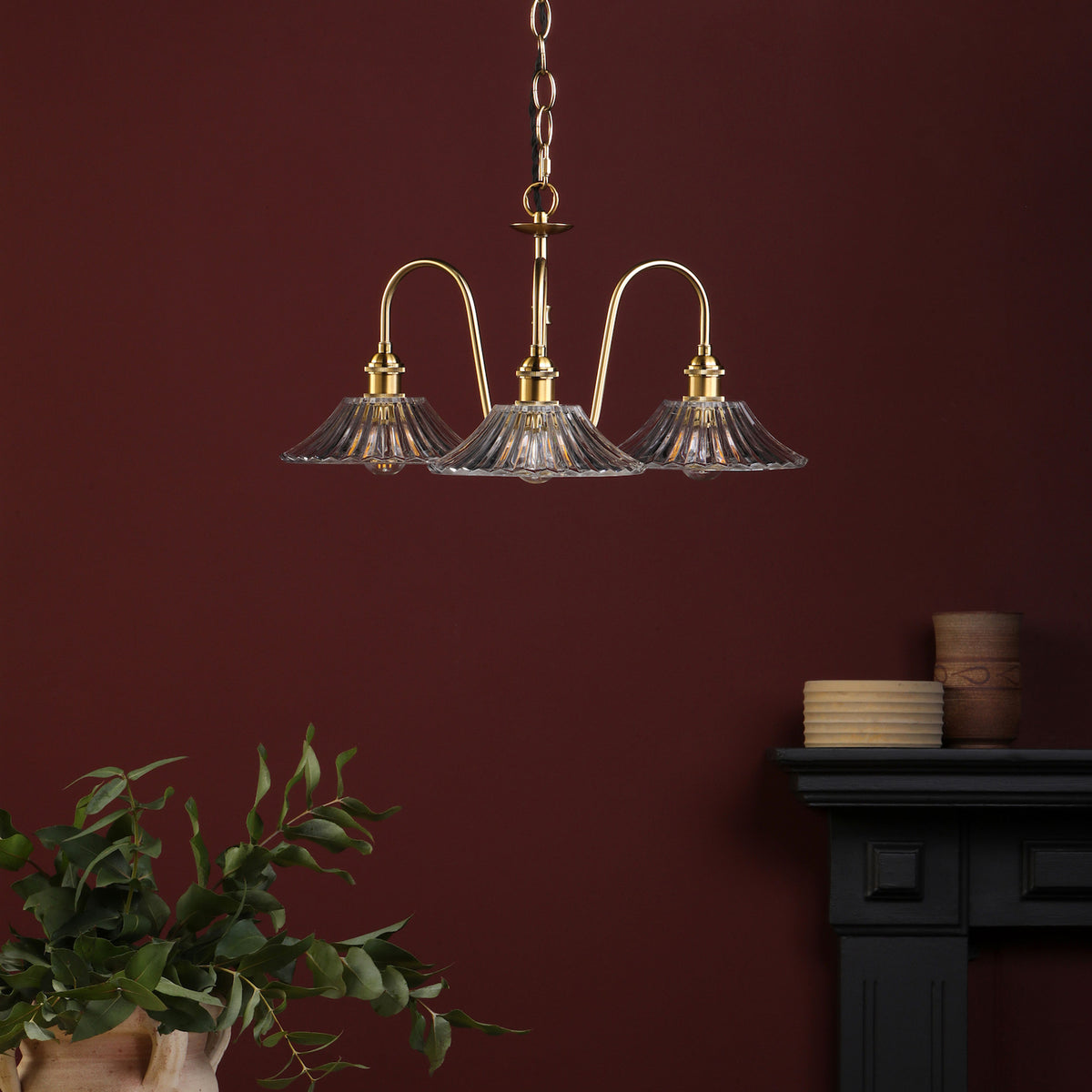 A three-arm brass chandelier with fluted glass shades hangs against a deep red wall.
