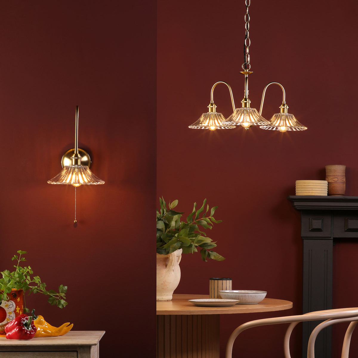 A brass wall sconce and a three-light chandelier with fluted glass shades illuminate a rich red room.