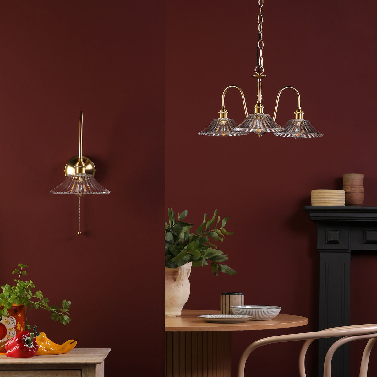 A brass wall light and a three-arm chandelier with ribbed glass shades against a deep red wall.