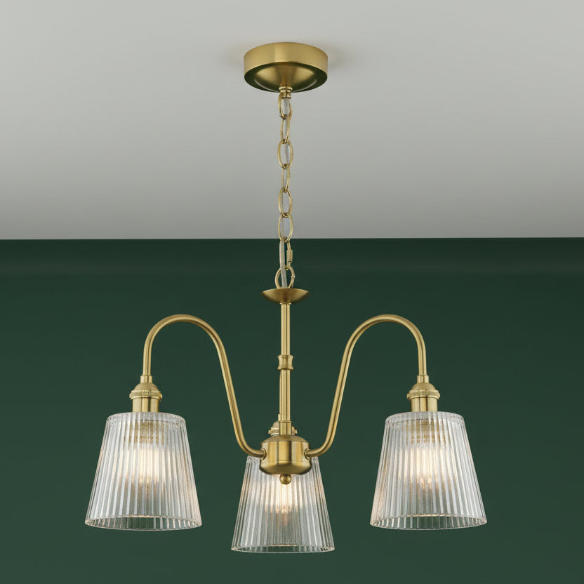 A three-light brass chandelier with ribbed glass shades, hanging from a chain and ceiling rose.