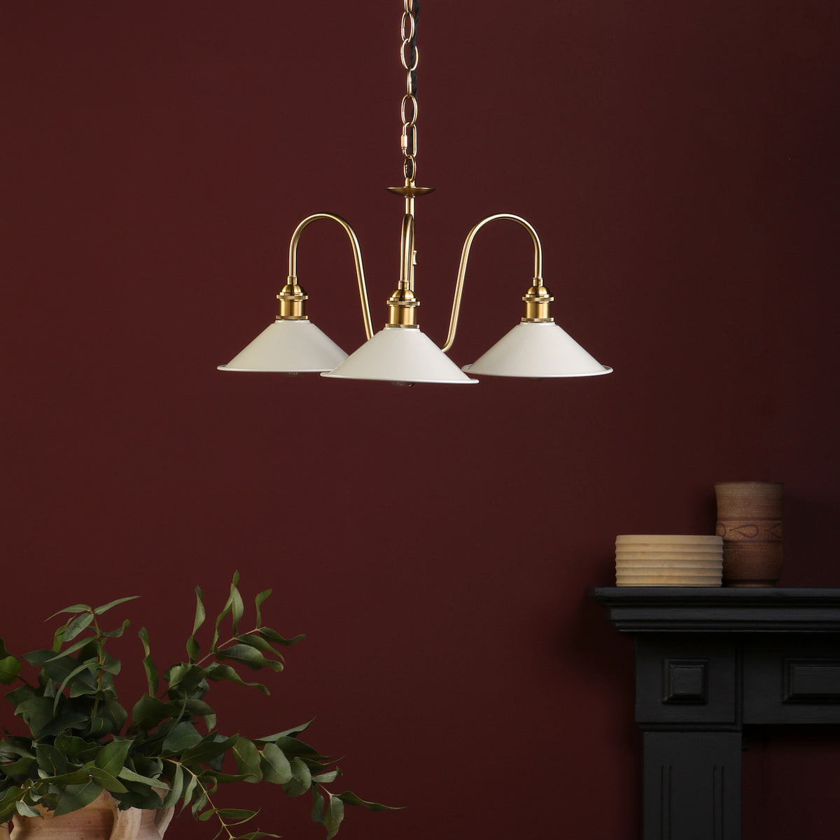 A three-arm ceiling light with white conical shades and brass accents hangs against a deep red wall.