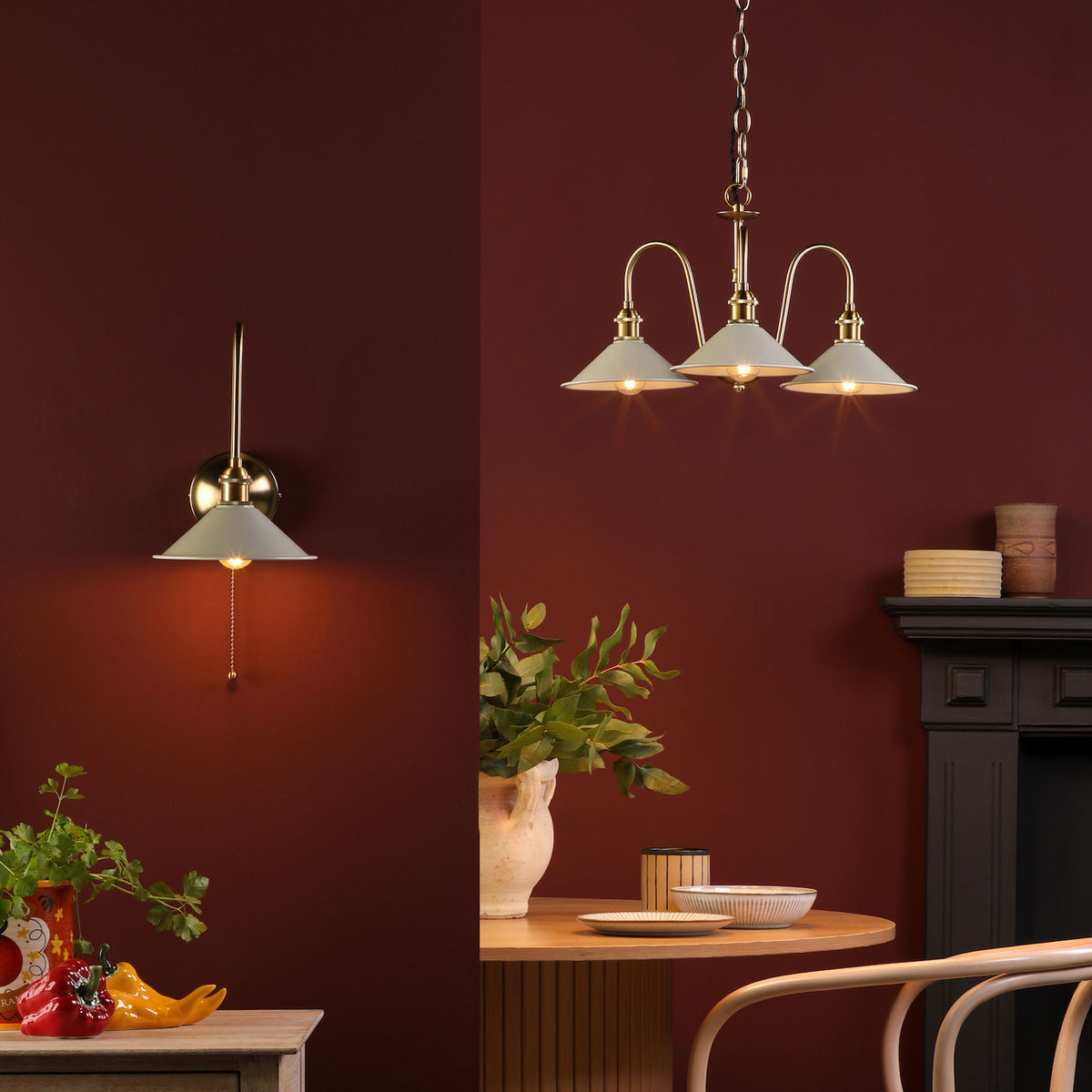 A wall sconce and a three-light chandelier with cream-colored shades illuminate a room with deep red walls.
