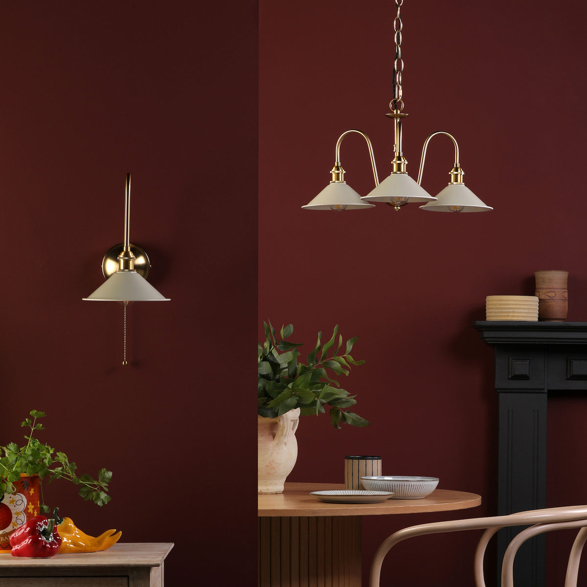 A brass wall sconce and a three-light chandelier with cream shades against a deep red wall.