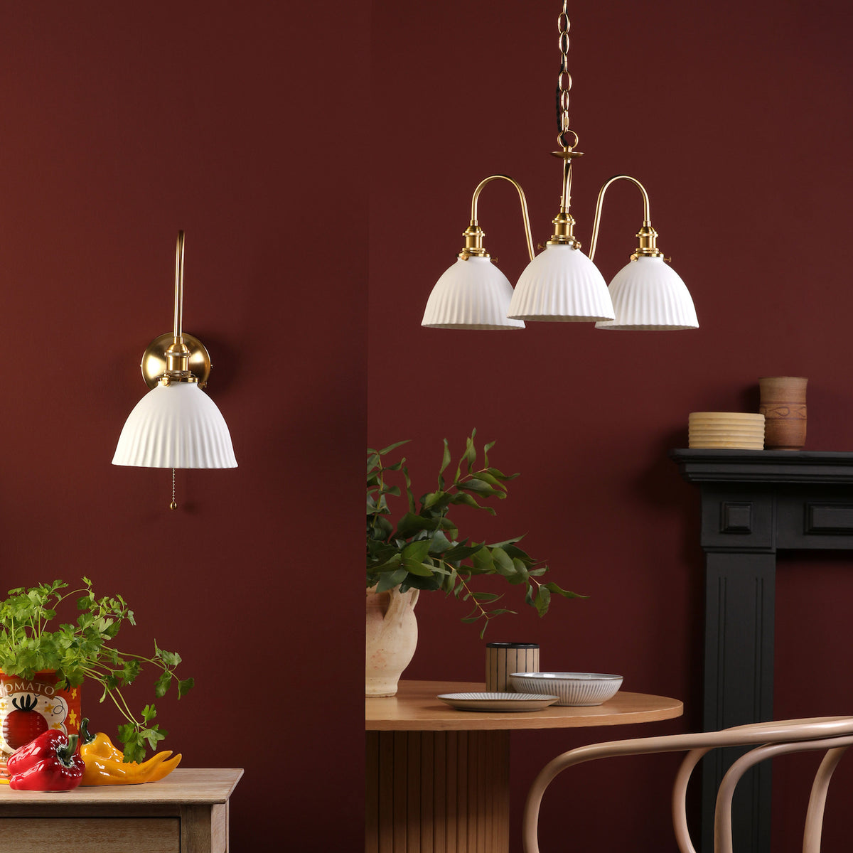 A brass wall light and a three-arm chandelier with white fluted shades against a deep red wall.