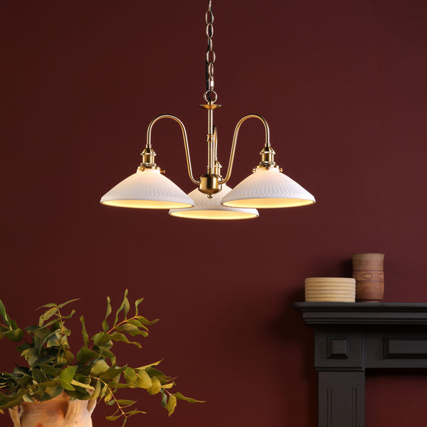 A brass chandelier with three white fluted shades hangs against a deep red wall.