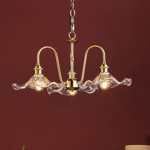 A three-light brass chandelier with wavy glass shades, illuminated against a deep red background.