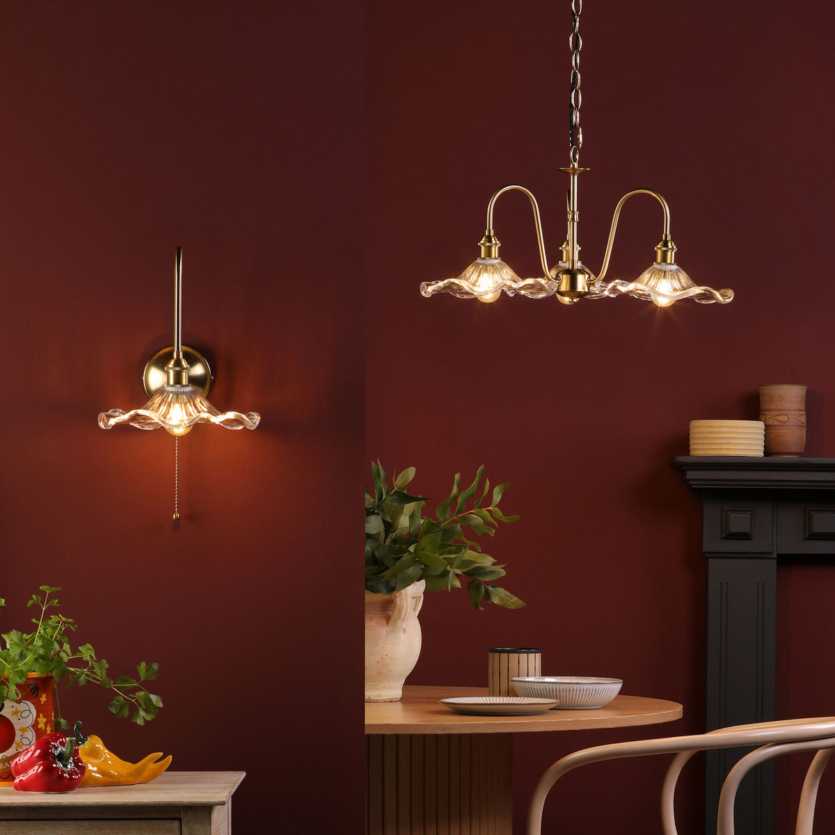 A brass wall sconce and chandelier with ruffled glass shades illuminate a dark red room.