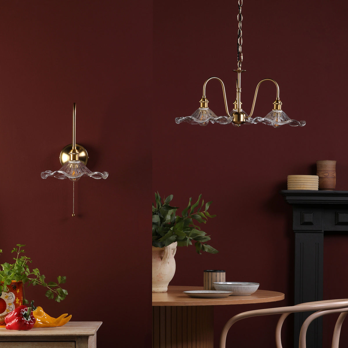 A brass wall sconce and chandelier with ruffled glass shades against a deep red wall.