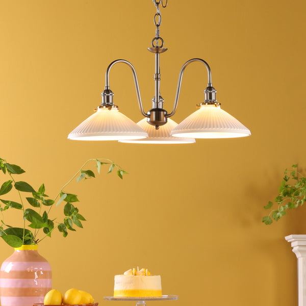 A three-light chandelier with fluted glass shades hangs from a chain against a yellow wall.