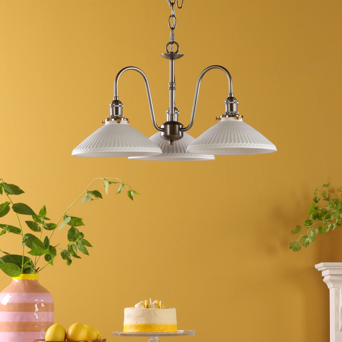 A three-light chandelier with white fluted shades hangs from a ceiling against a yellow wall.