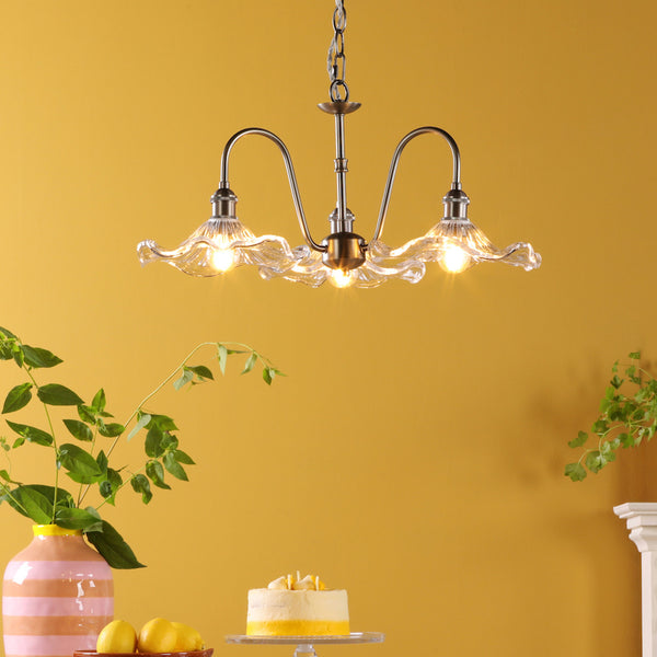 A three-light chandelier with clear, wavy glass shades hangs from a chain against a yellow wall.