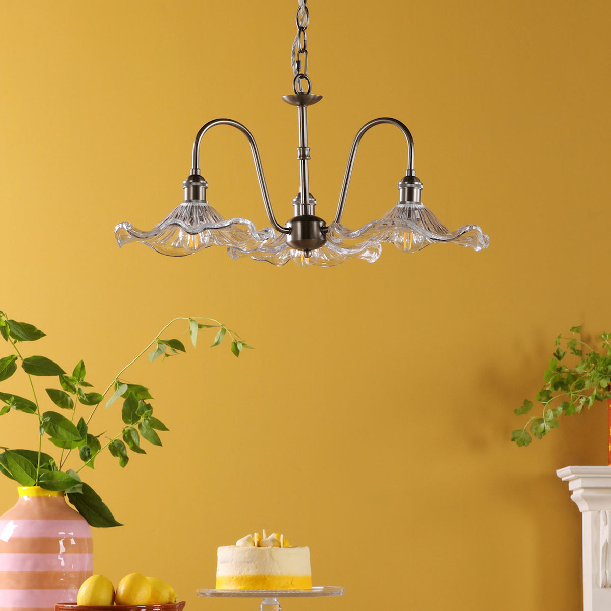 A three-light chandelier with clear, ruffled glass shades hangs from a mustard yellow ceiling. 