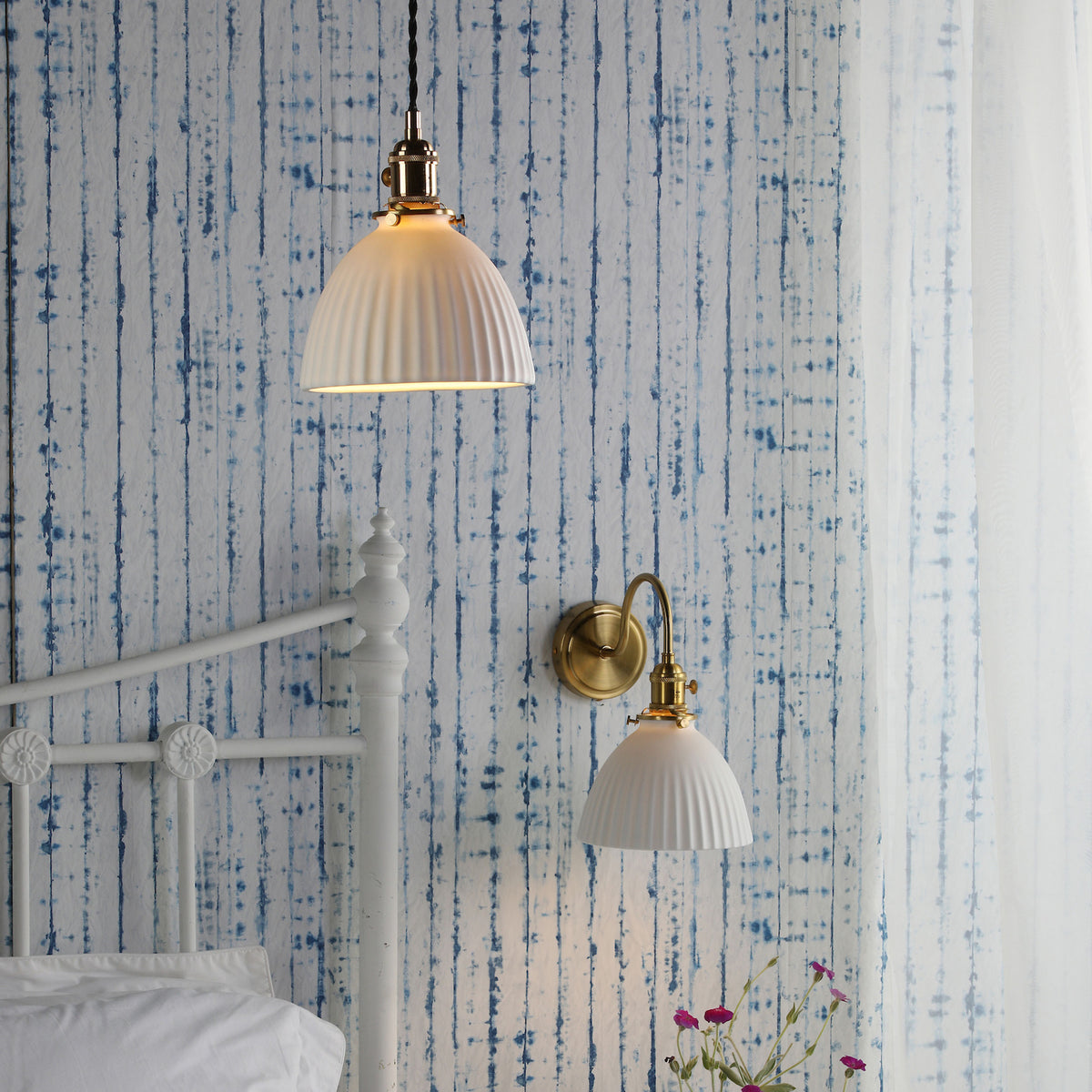 Bedroom with blue and white striped wallpaper, white metal bed frame, and two brass and white ceramic lights.