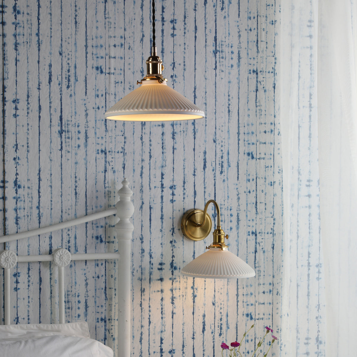 Two white pleated ceramic lights with brass fittings, one pendant and one wall-mounted, against a blue tie-dye wall.