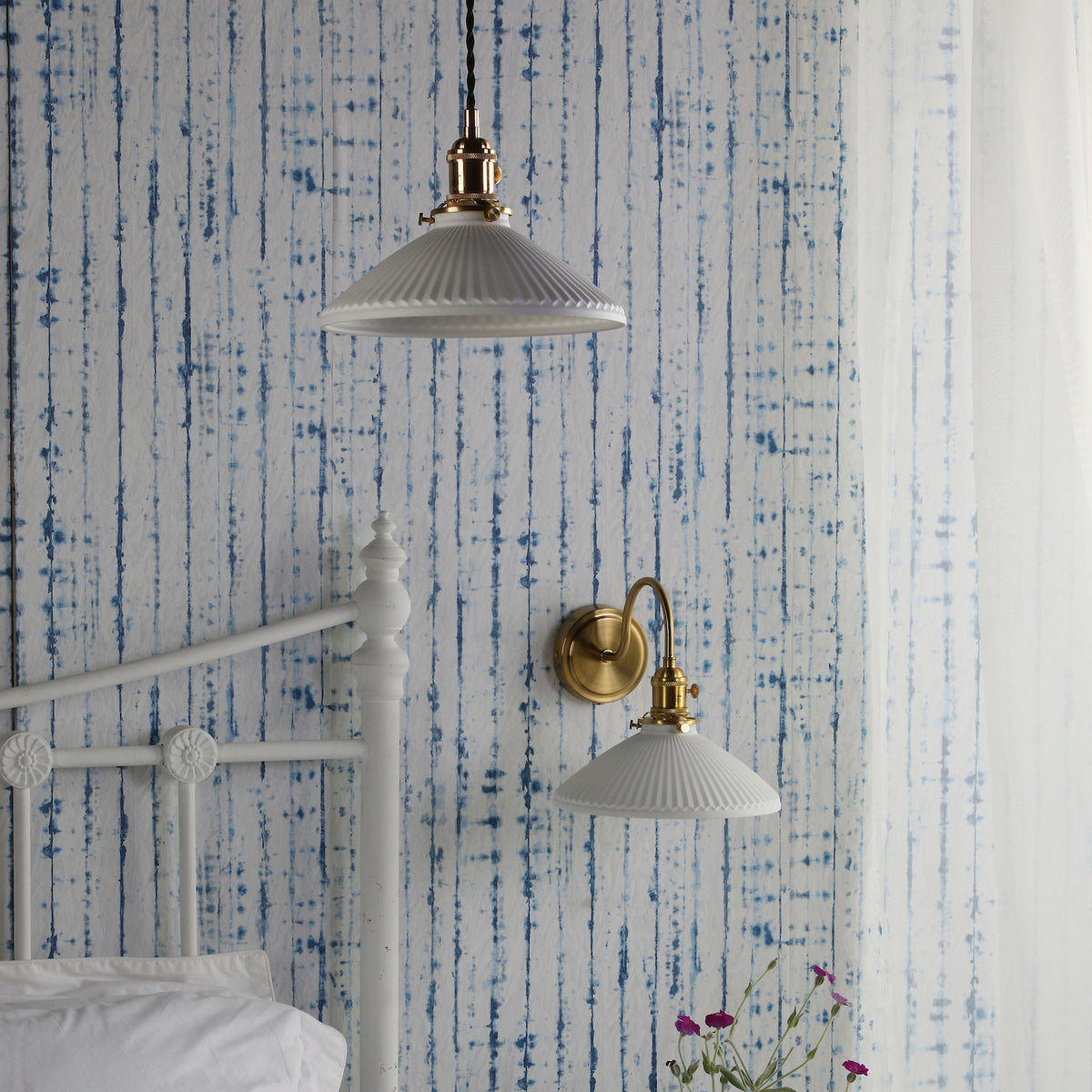 Bedroom with white metal bed frame, blue and white striped wallpaper, and two white fluted glass lights.