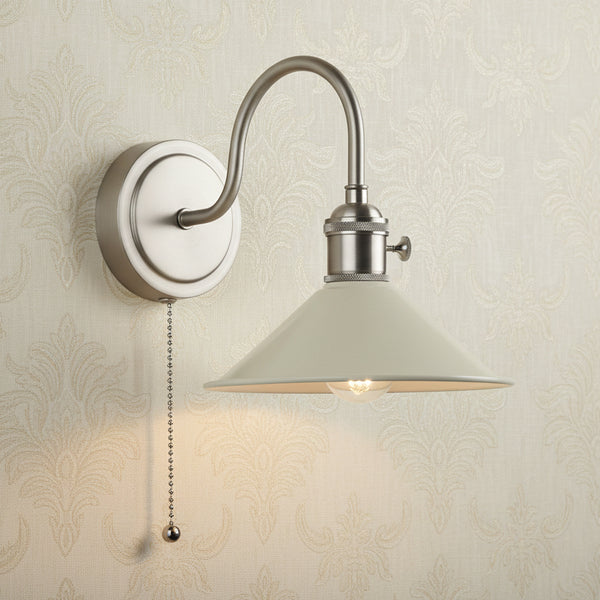 Brushed nickel wall sconce with a curved arm, a cream-colored conical shade, and a pull chain.
