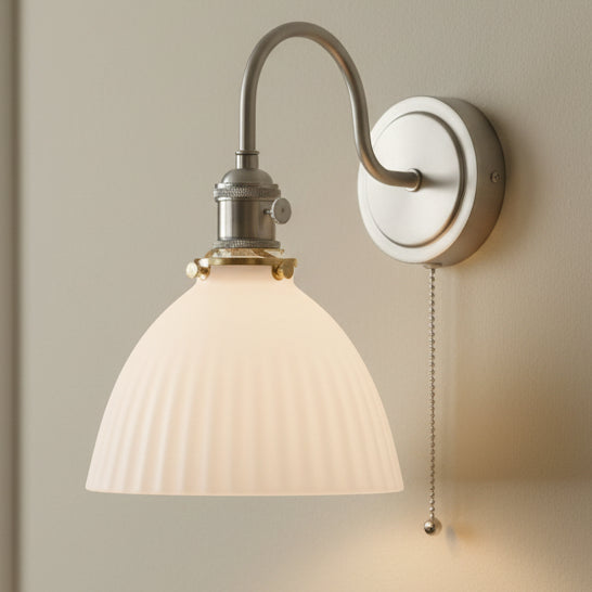 Brushed nickel wall sconce with a curved arm, a ribbed white glass shade, and a pull chain.