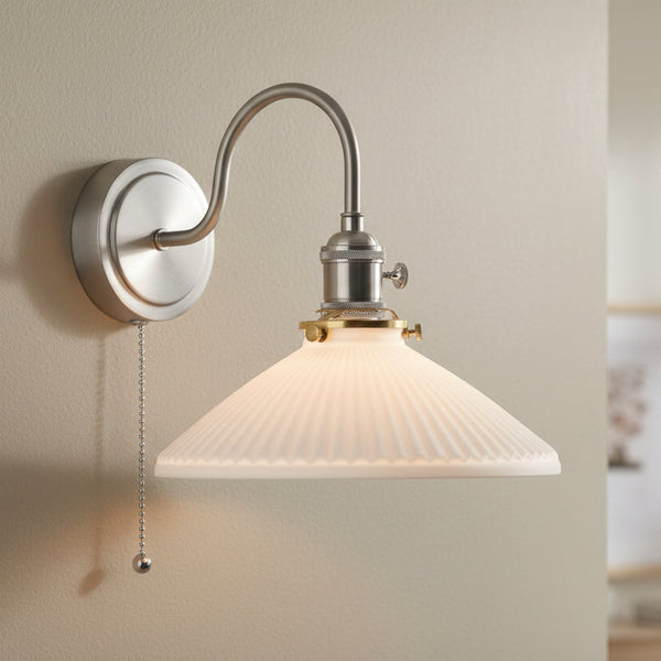 Brushed nickel wall sconce with a curved arm, a ribbed white glass shade, and a pull chain switch.