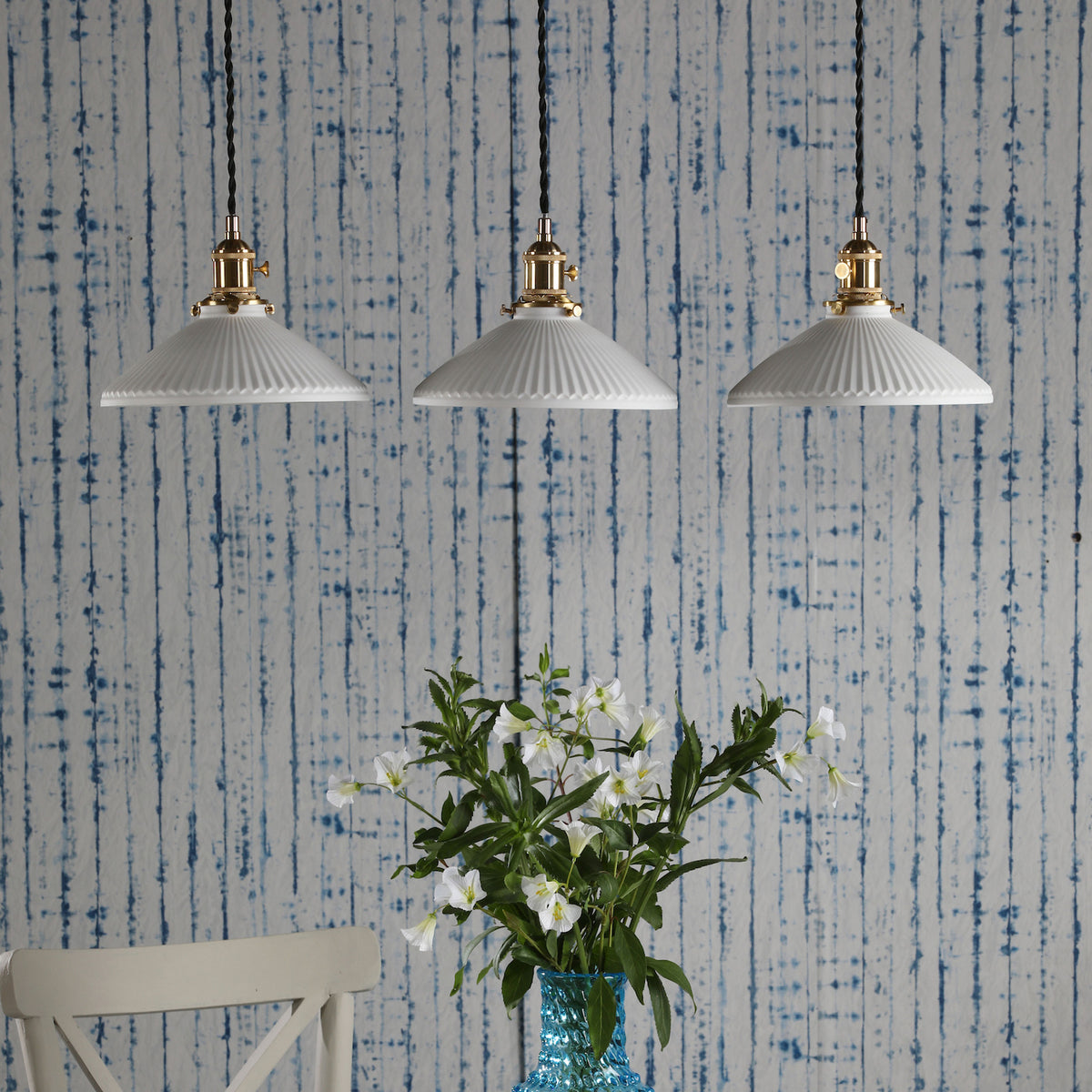 Three white fluted pendant lights with brass fittings hang against a blue and white striped wall.
