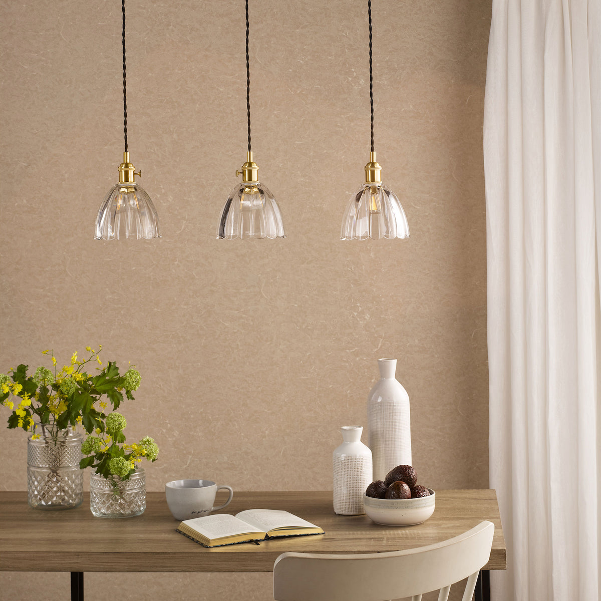 Three clear glass pendant lights with brass fittings hang above a wooden table.