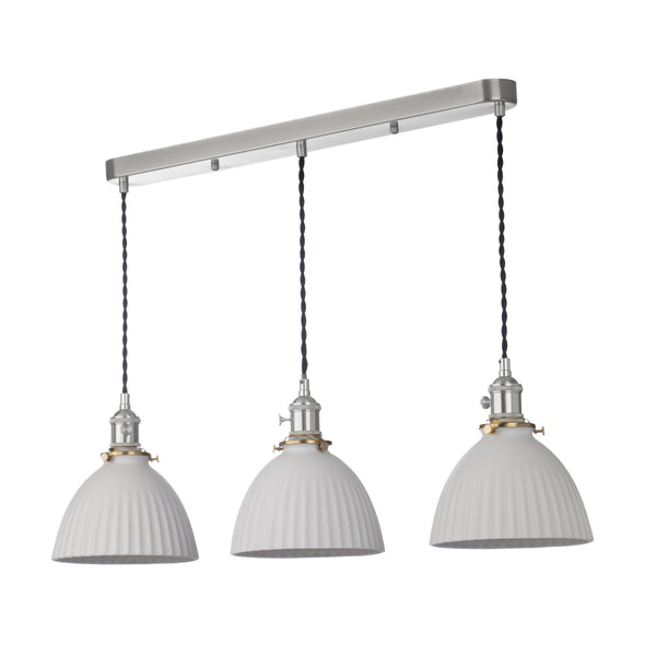 Three white fluted pendant lights hang from a brushed nickel bar, with black braided cords and brass accents.