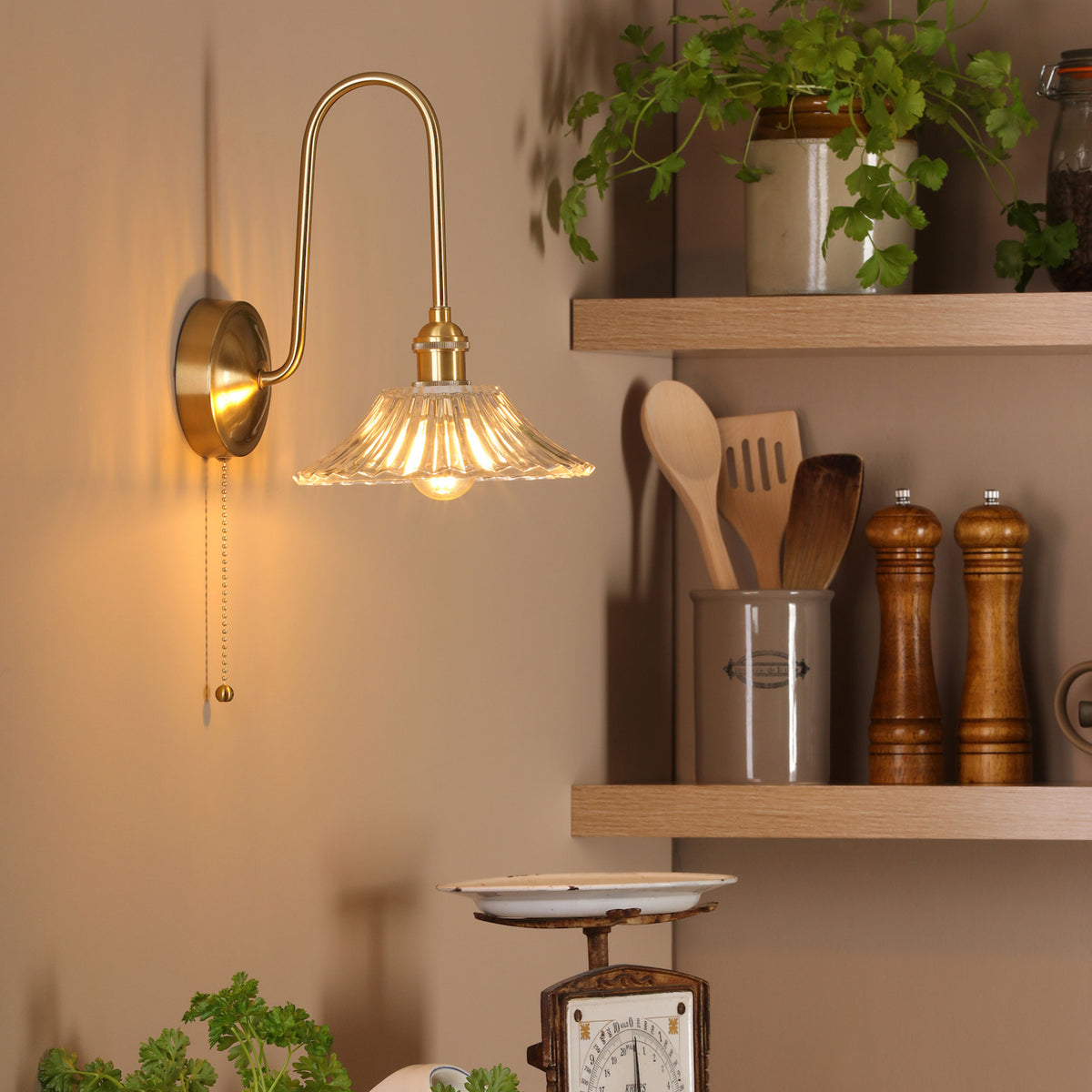 A brass wall light with a fluted glass shade illuminates a kitchen wall with wooden shelves.