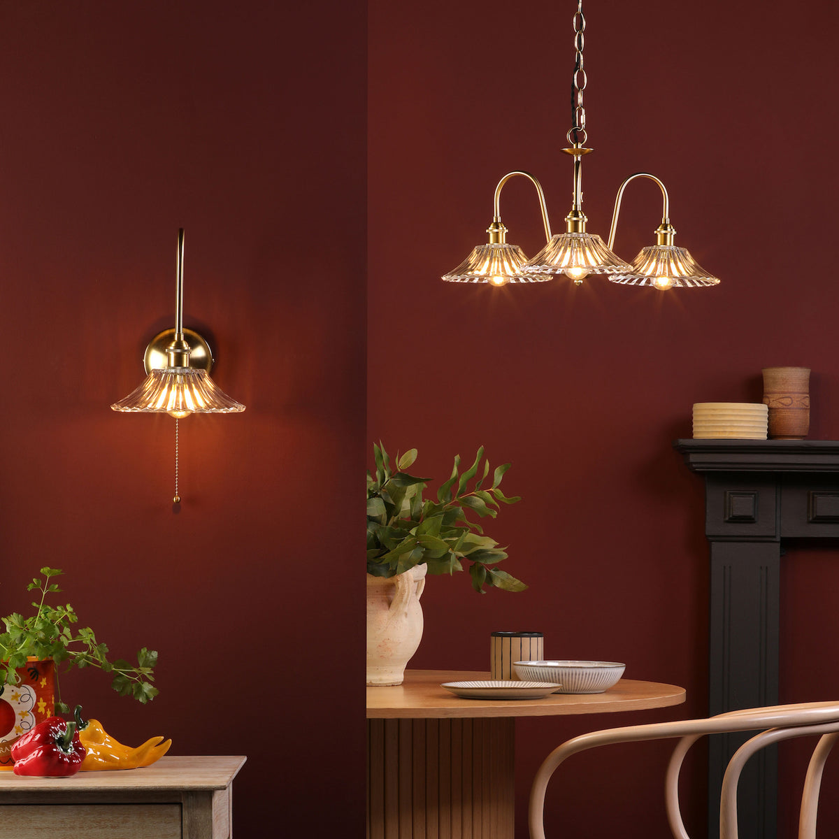 A brass wall sconce and a three-light chandelier with fluted glass shades illuminate a deep red room.