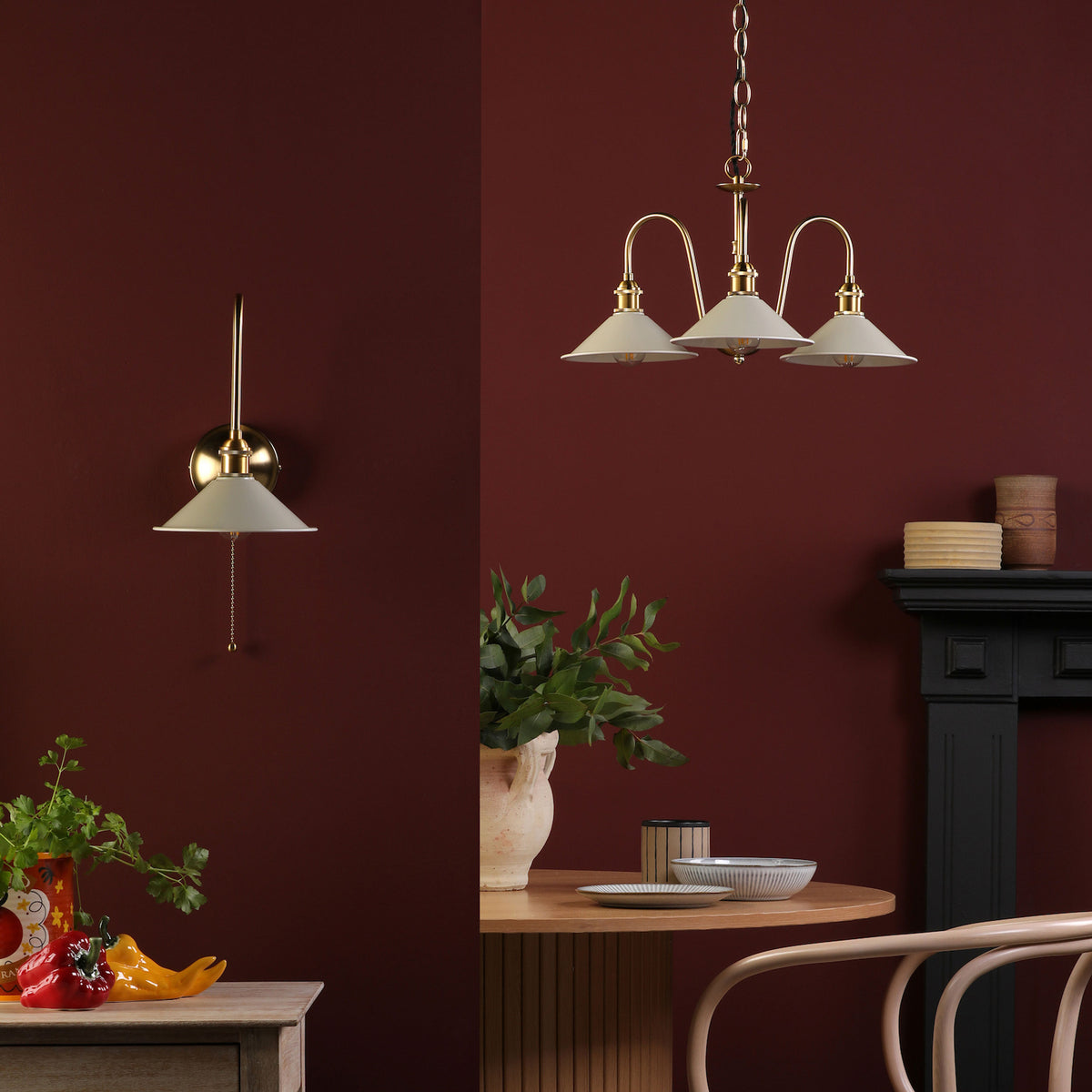 A brass wall light and a three-arm chandelier with cream shades against a deep red wall.