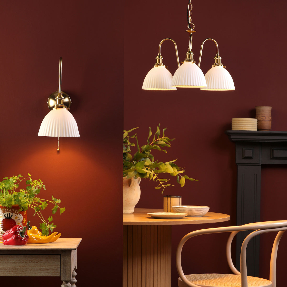 A wall sconce and a three-light chandelier with pleated white shades illuminate a room with deep red walls.