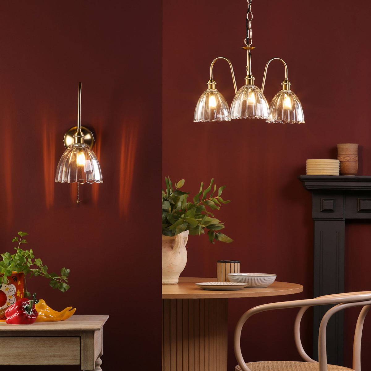 A wall sconce and a three-light chandelier with clear, fluted glass shades illuminate a rich red room.