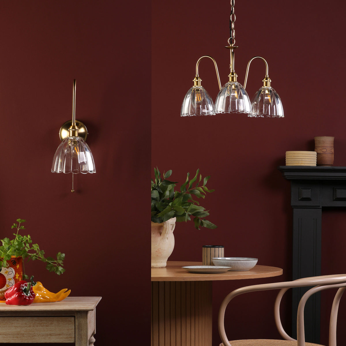 A brass wall sconce and a three-light chandelier with fluted glass shades in a room with a dark red wall.