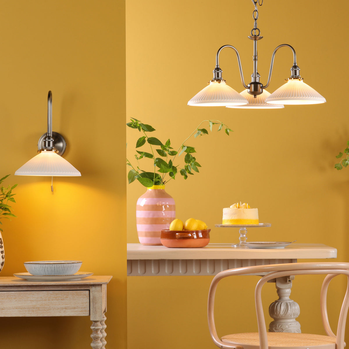 A dining room with yellow walls, a wall sconce, and a chandelier with pleated glass shades.