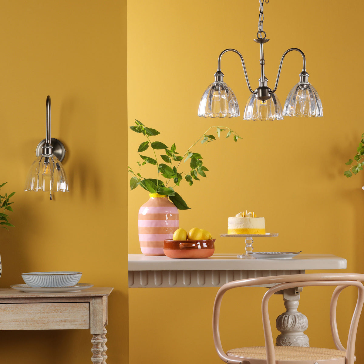 A room with mustard yellow walls, featuring a wall light and a three-arm chandelier with fluted glass shades.
