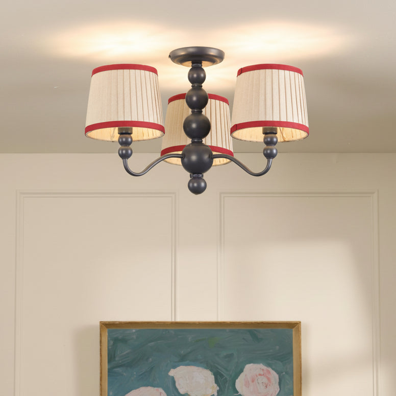 Three light semi flush mount ceiling light with cream pleated shades and red trim on a dark central spindle