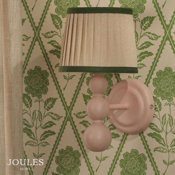Joules Harewood wall light in matt pink with a pleated linen shade mounted on green floral wallpaper